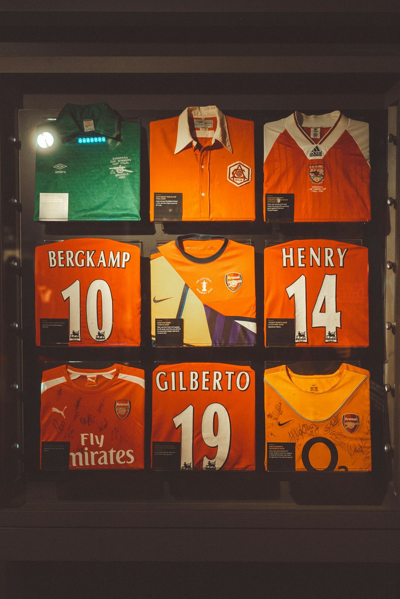 Arsenal football jerseys are displayed in a glass case.